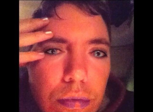 A person looks into a front facing camera screen. Their face has computer-generated filters imposed overtop that change the lip shade, foundation or skin colour and eye colour, eye makeup, and nails. The person has short hair, fair skin and wears a hoodie.