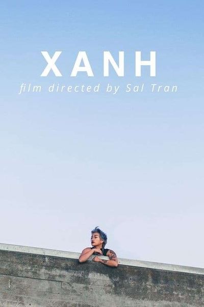 A person leaning on a concrete wall with a skyline above them.They have light brown skin with tattoos on their right arm. They are wearing a black tank top and a gold chain around their neck. They have short light blue hair and are wearing lipstick looking off to the left. In the skyline above the person, white text reads "XANH: film directed by Sal Tran."